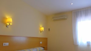 Une chambre d’hôtel comprenant un lit, des tables de chevet, des lampes fixées au mur, un appareil de climatisation et une fenêtre avec des rideaux.