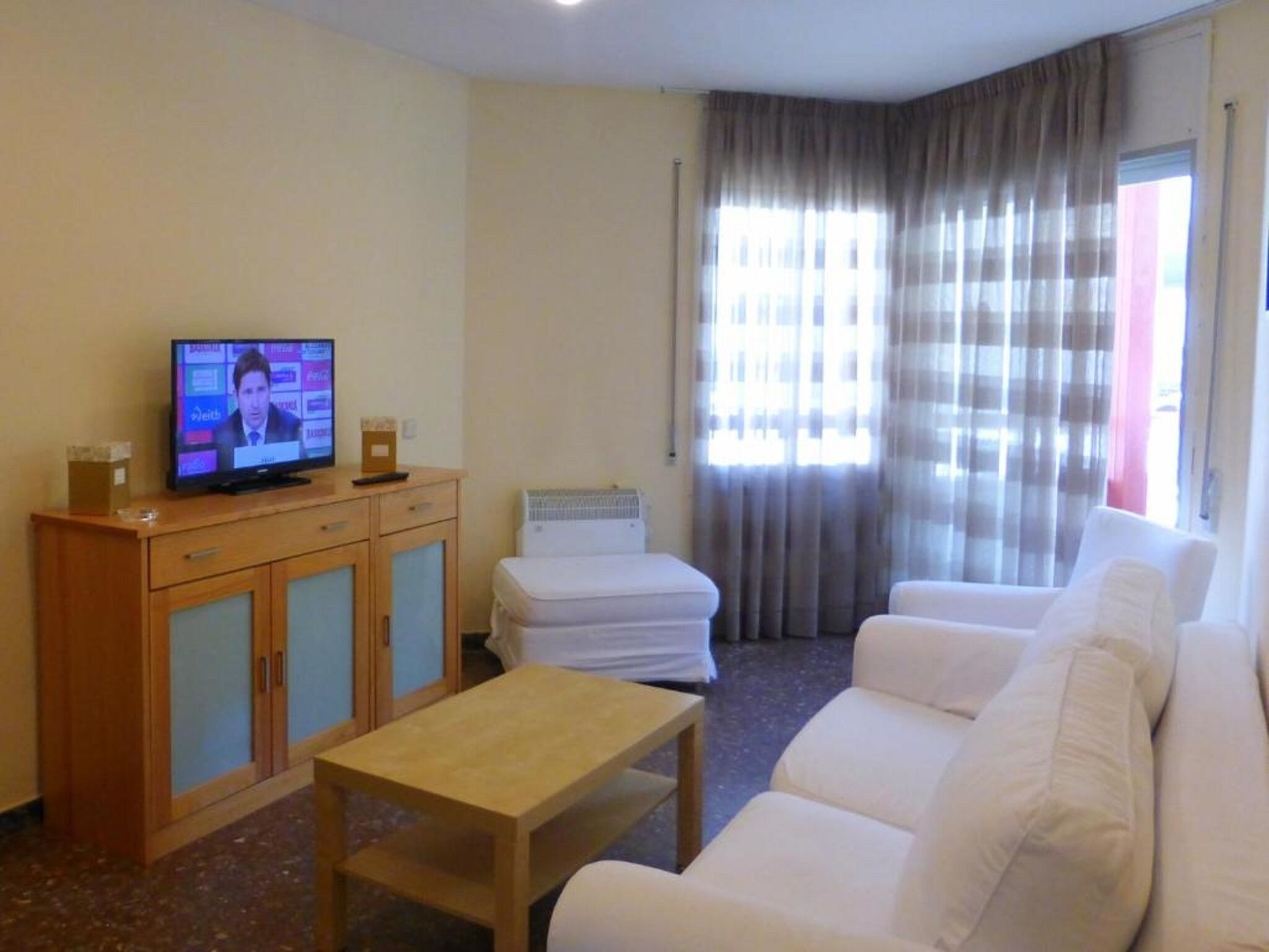 Un salon avec un téléviseur, un meuble en bois, un canapé blanc et une petite table.