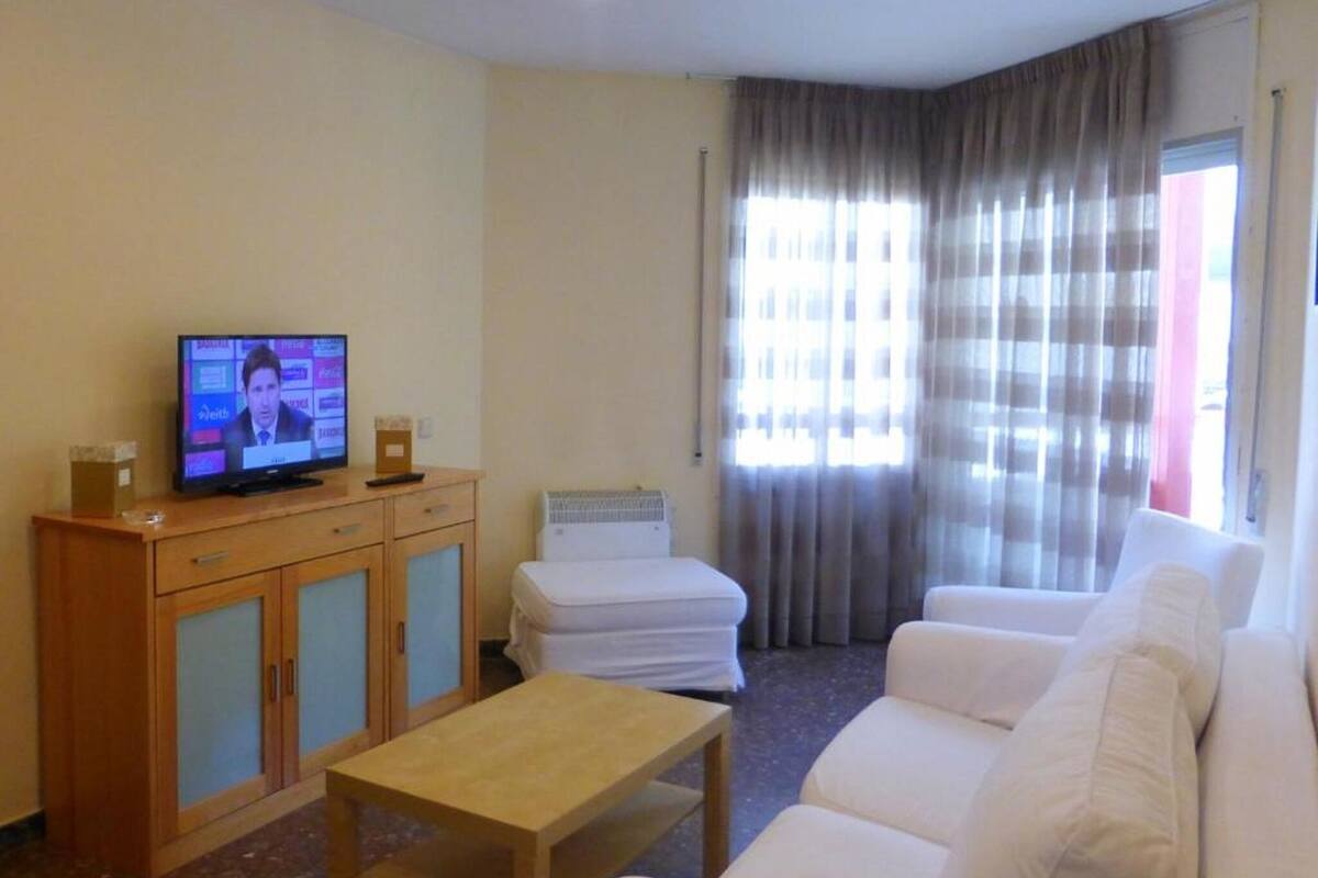 Una sala de estar con televisor, un mueble de madera, un sofá blanco y una mesita.