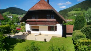 Een huis in chaletstijl met een schuin dak, een balkon en een verzorgde tuin.