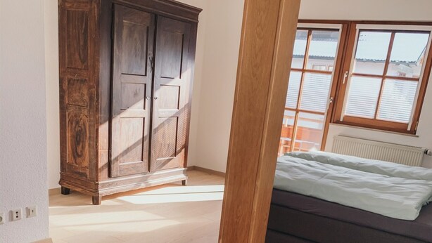 Een slaapkamer met een bed, een houten garderobe en uitzicht op het omliggende landschap.