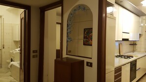 Une cuisine moderne avec des meubles blancs, une cuisinière à gaz et un évier. Un arc décoratif orne le mur, et un tableau est accroché au-dessus de l’évier.