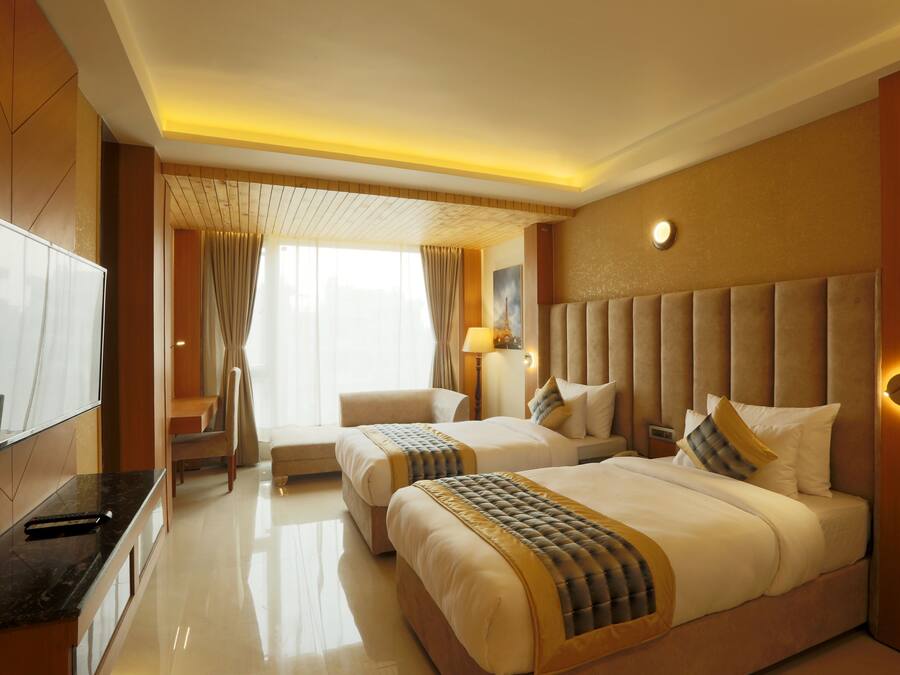 A hotel room with two beds, a TV, a desk, and a bathroom.