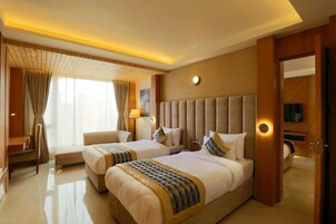 Habitación de hotel con dos camas, un escritorio, una silla y un ventanal con cortinas.