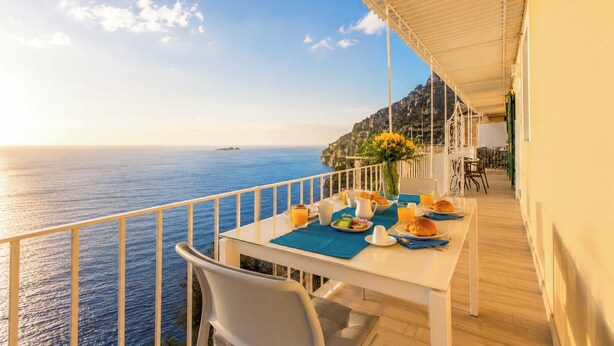 En balkon med et bord dækket til morgenmad, med udsigt over havet.