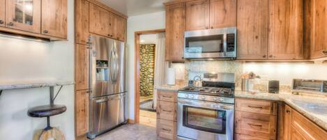 A kitchen with wooden cabinets, stainless steel appliances, a stone wall, and a stool.