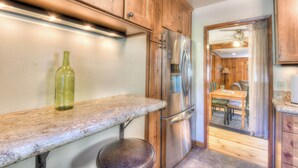 A kitchen with wooden cabinets, a stainless steel refrigerator, a marble countertop, and a dining area visible through an open doorway. - Moonlight Cove w/ Grill Tahoe Beach Next Door! (Kings Beach)