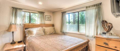 Un dormitorio con una cama de madera, una mesita de noche con lámpara, un aparador y una ventana con cortinas.
