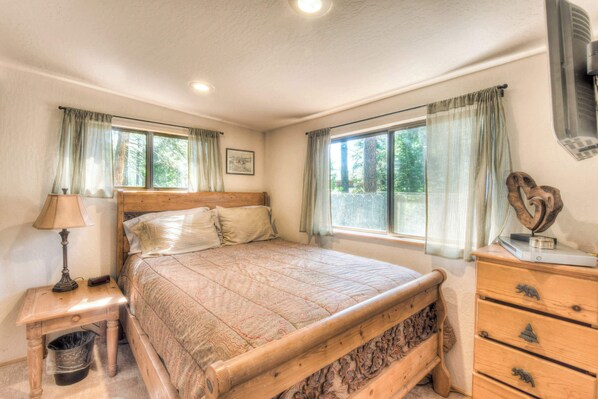A bedroom with a wooden bed, a nightstand with a lamp, a dresser, and a window with curtains. - Moonlight Cove w/ Grill Tahoe Beach Next Door! (Kings Beach)