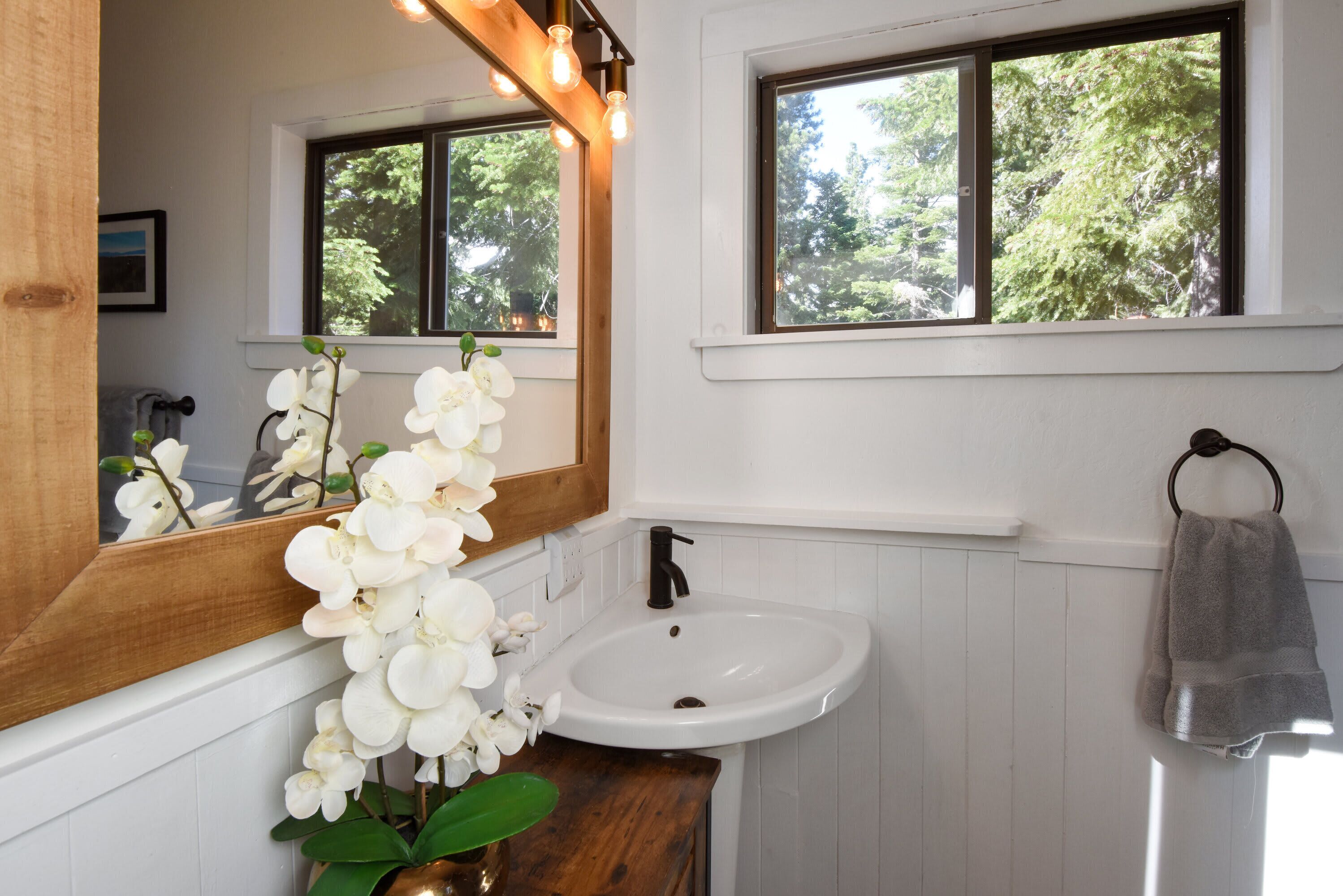 Un bagno con un lavandino bianco, uno specchio e una finestra vista alberi.