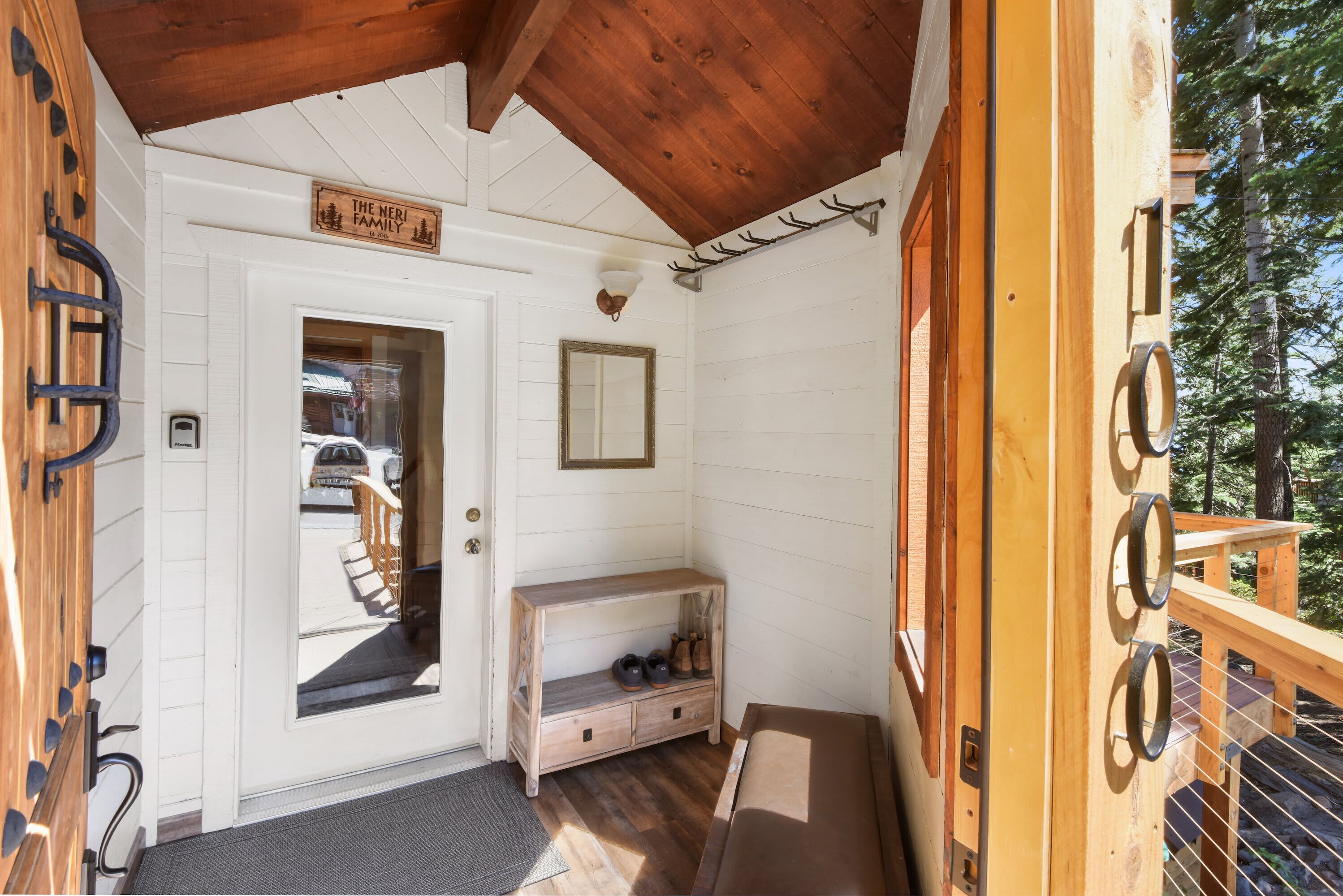 L’entrée d’un chalet en bois, avec une porte, un banc où sont posées des chaussures et une pancarte sur laquelle on peut lire : « La famille joyeuse ».
