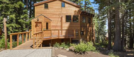 Une cabane en bois avec un escalier menant à une terrasse, entourée d’arbres.