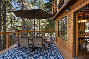 A wooden deck with a dining table and chairs, surrounded by tall trees.