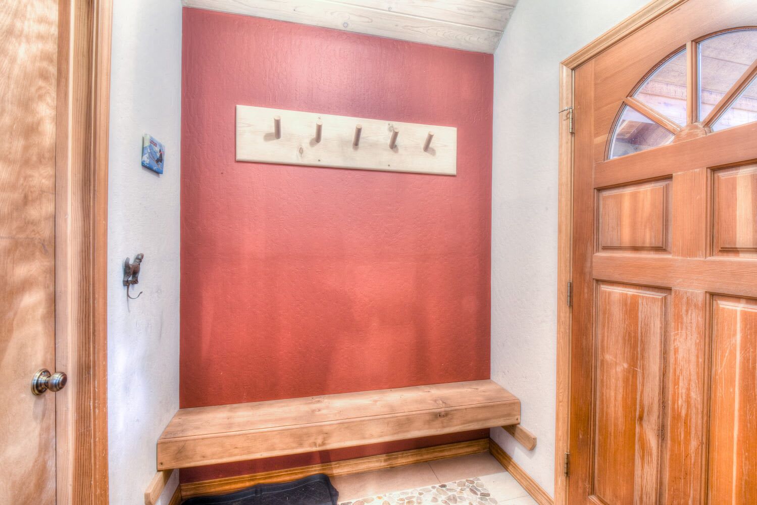 Eine Holztür mit Fensterglas, eine rote Wand und eine Holzbank.