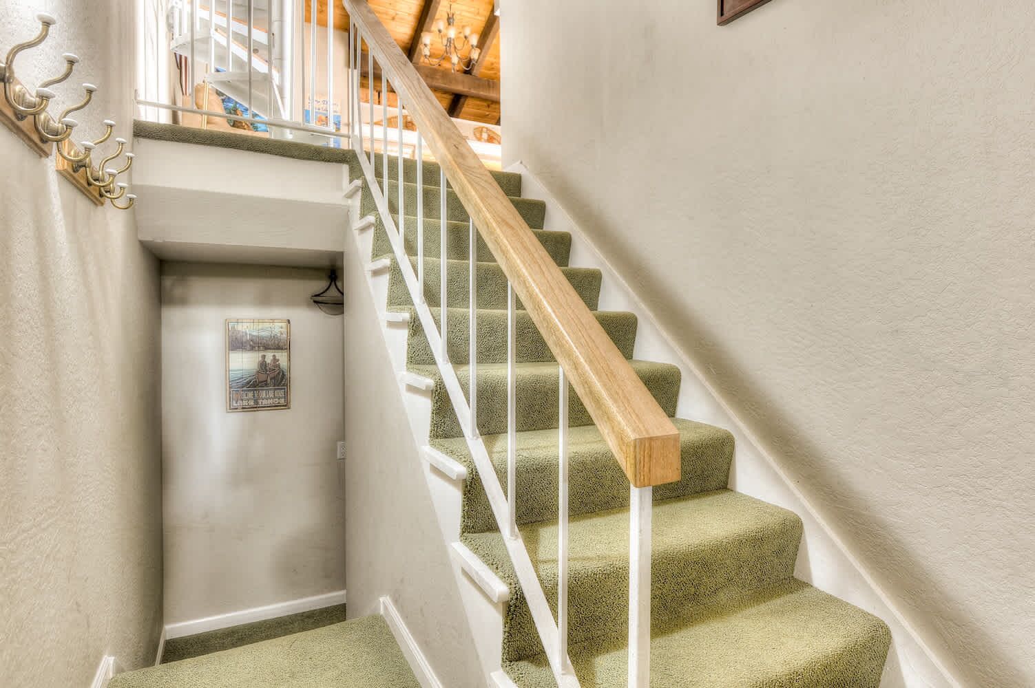 A staircase with green carpeted steps and white railings, leading to a landing with a door and a framed picture.