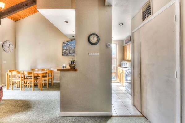 A hallway with a wooden dining table and chairs, a clock on the wall, and a view into a kitchen area. - Lake Forest Villa Patio w/ BBQ (Tahoe City)