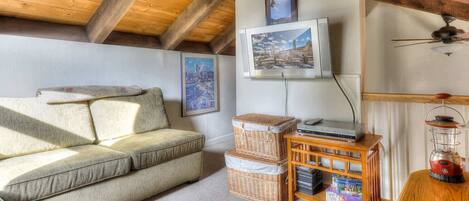 A cozy living room with a sofa, a television, and a wooden ceiling.