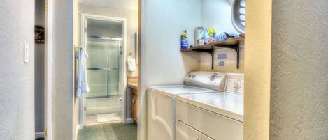 A laundry area with a washing machine, a dryer, and a shelf with cleaning supplies.