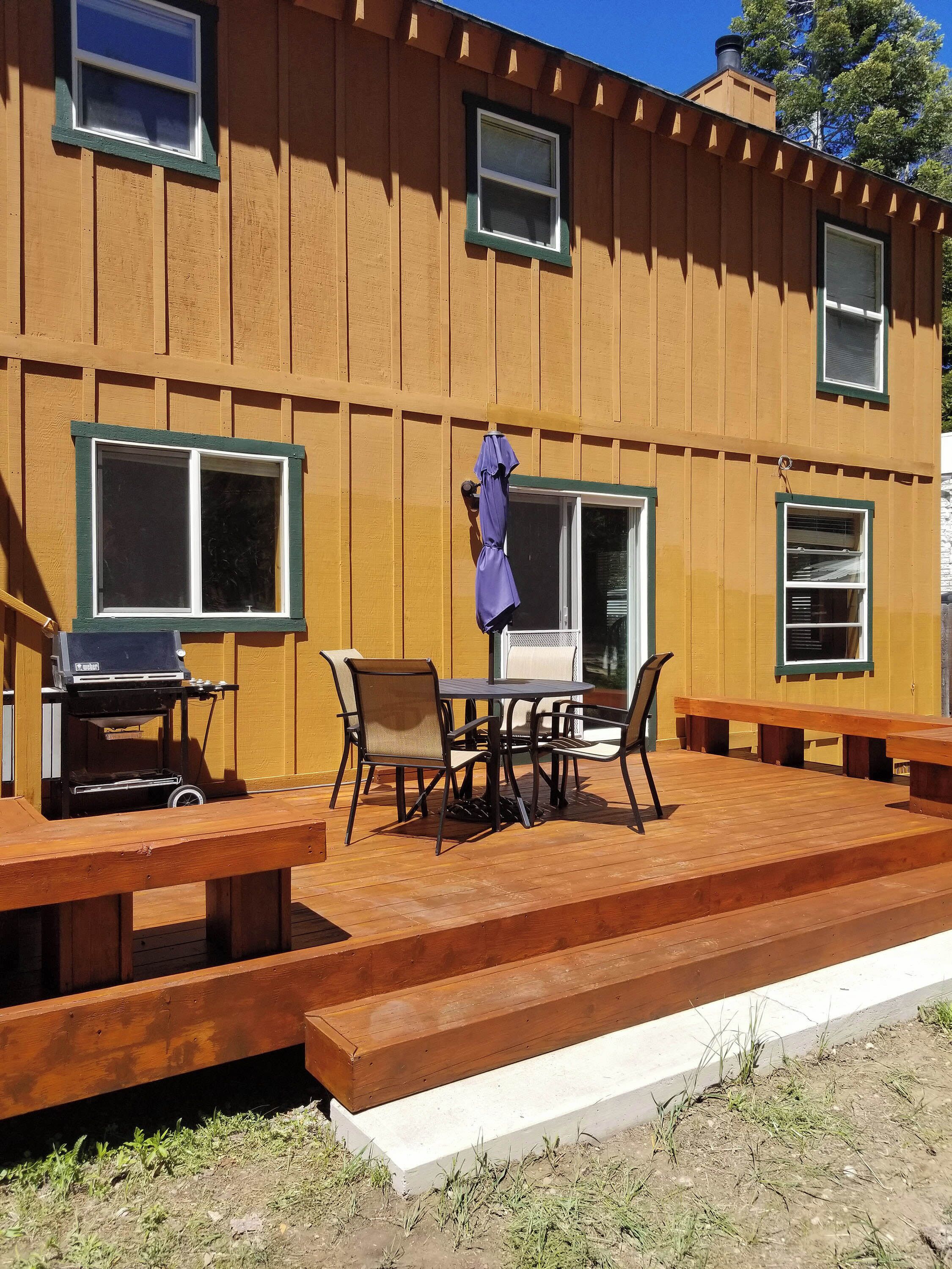 A wooden deck with outdoor furniture, a grill, and multiple windows.