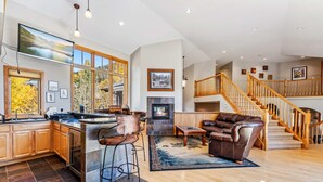 A spacious living area with a fireplace, a large island with bar stools, wooden flooring, and a staircase leading to an upper level. - Massive Breckenridge Estate: Game Room & Hot Tub! (Breckenridge)