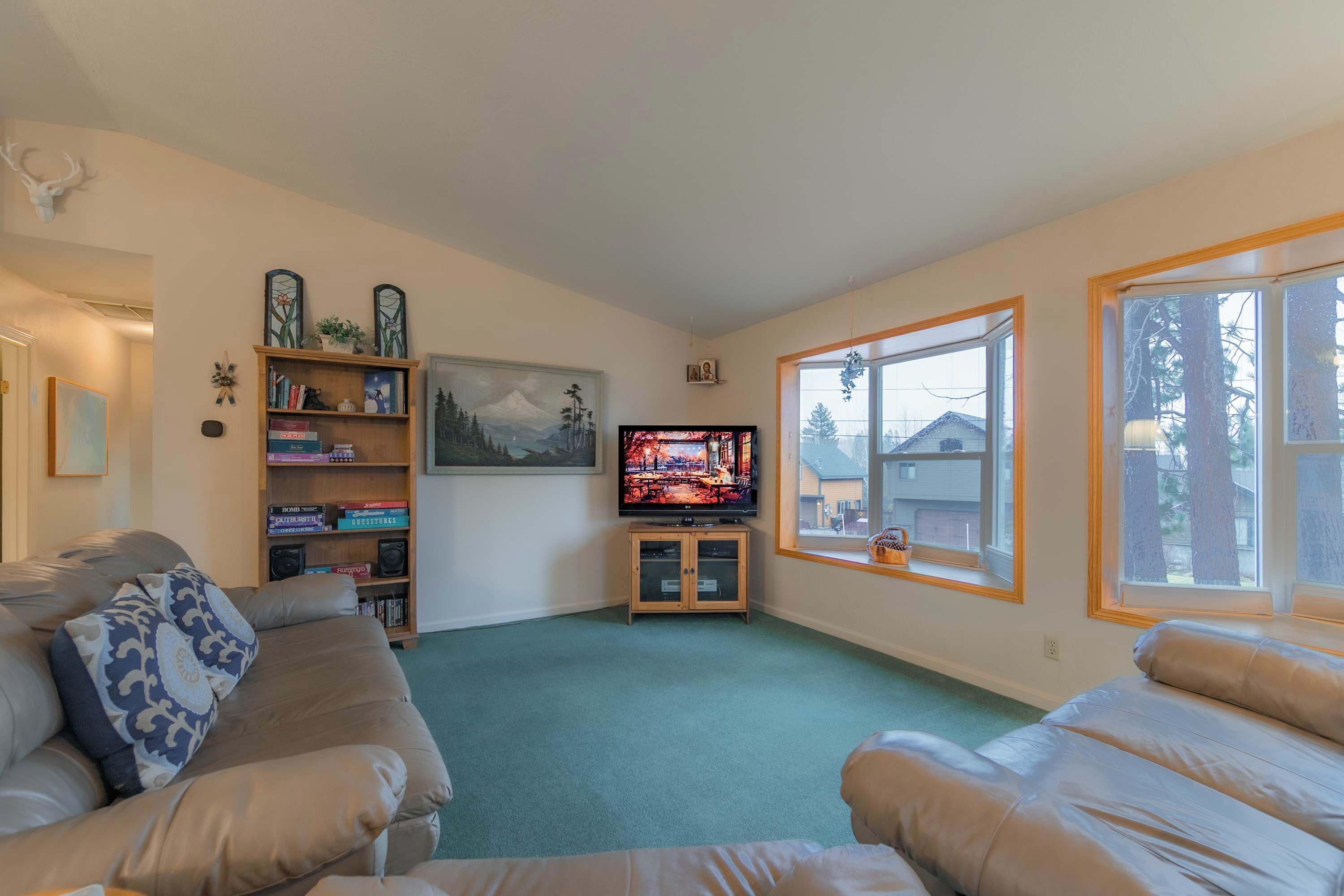 A living room with a beige sofa, a television, a bookshelf, and a window with a view of trees.