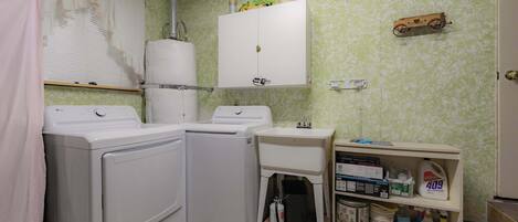 Un área de lavandería con dos lavadoras, un lavabo y un estante con productos de limpieza.