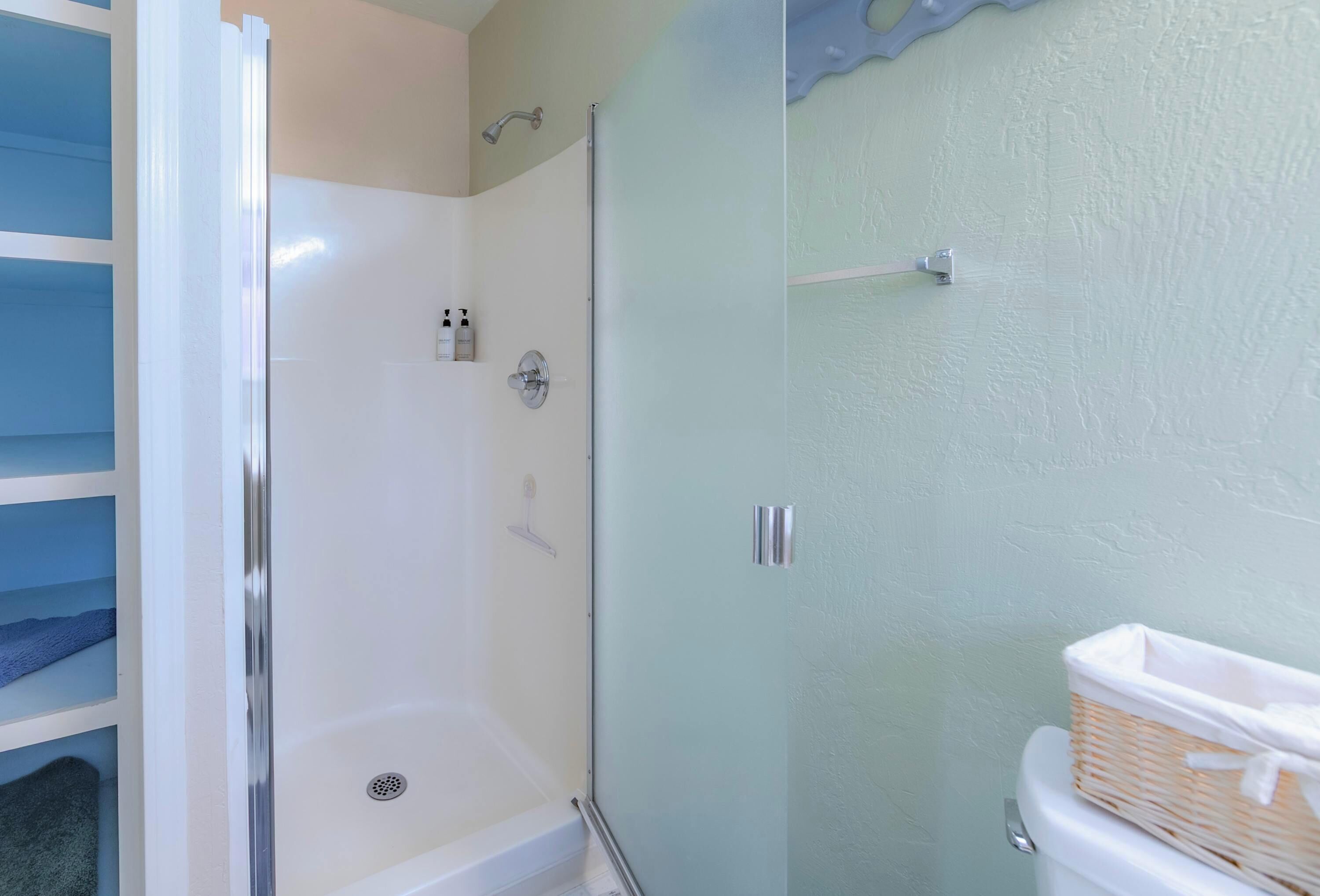 Een badkamer met een douchecabine van glas, een witte badkuip en een toilet met een rieten mandje.