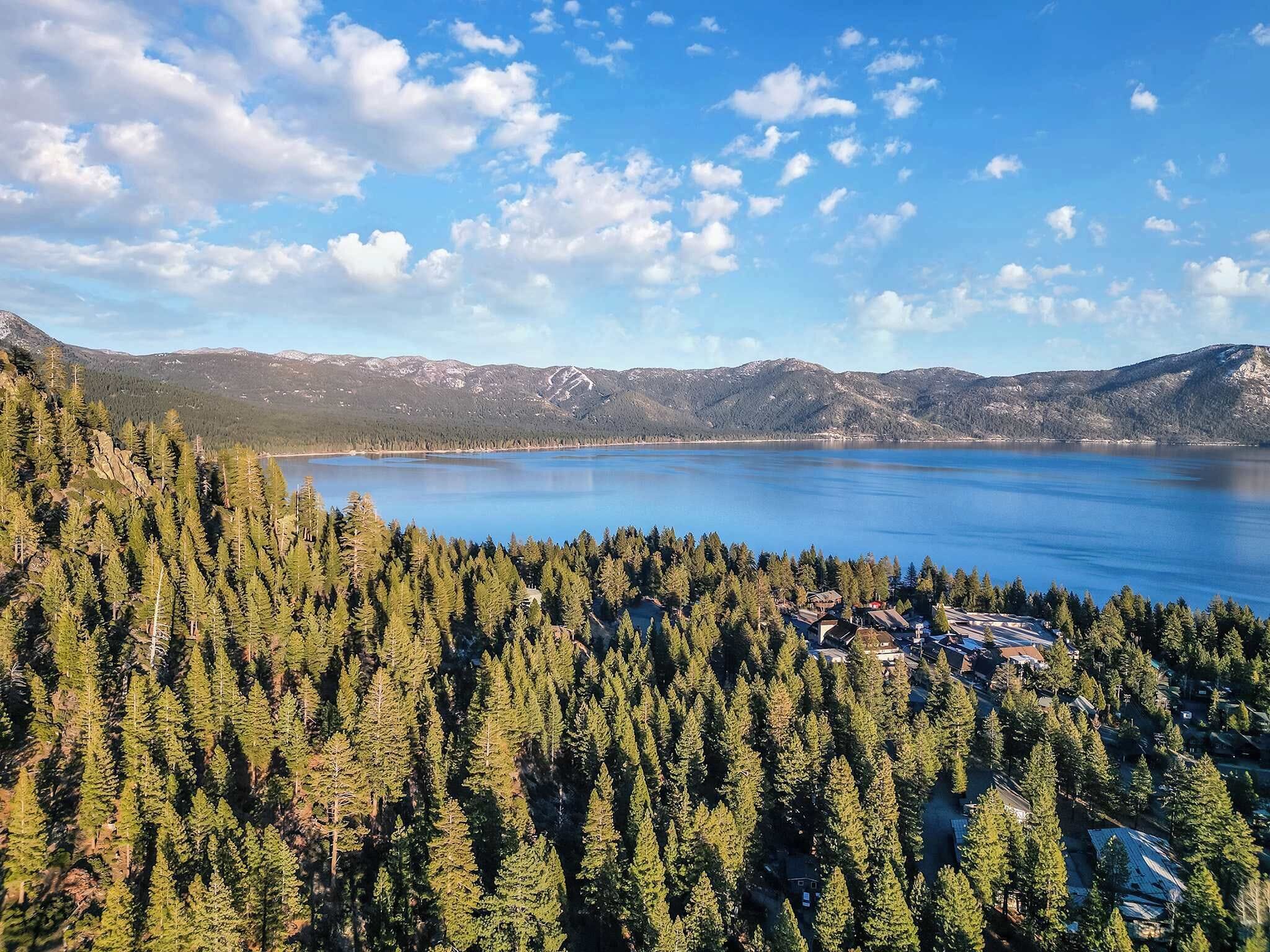 Paisaje montañoso con un lago, denso bosque y un pequeño poblado con edificios.