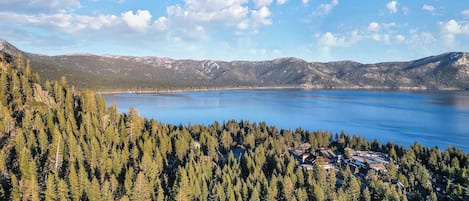 Paisaje montañoso con un lago, denso bosque y un pequeño poblado con edificios.
