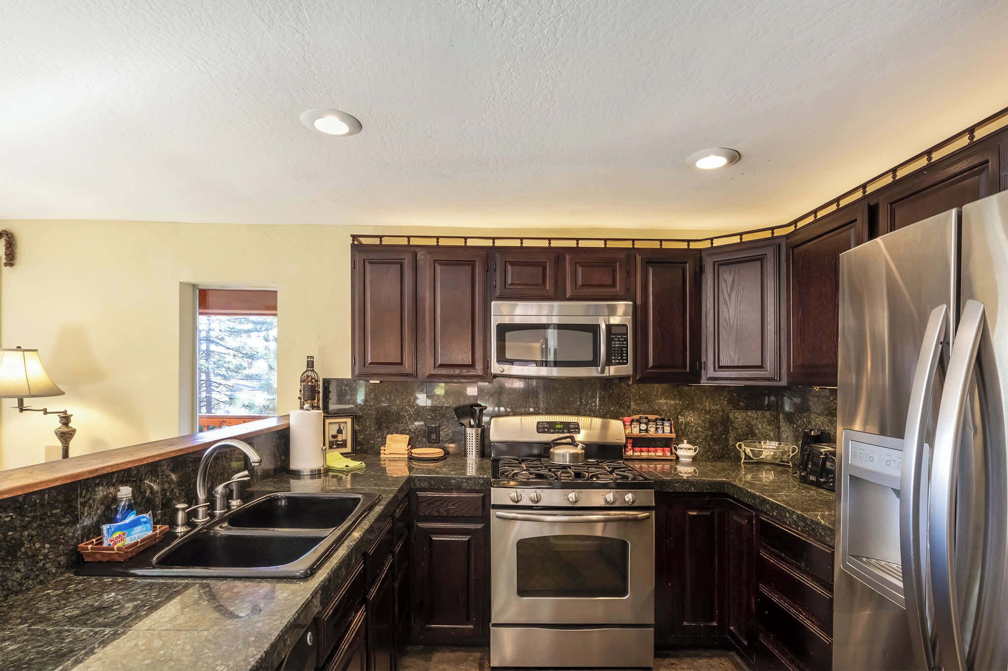 A modern kitchen with dark wood cabinets, stainless steel appliances, granite countertops, and a window providing natural light.