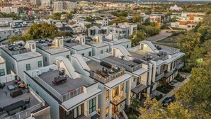 Un moderno complejo de apartamentos con múltiples unidades, terrazas en la azotea y una combinación de edificios residenciales y comerciales al fondo.
