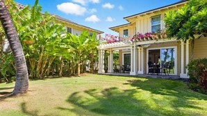 Et toetagers hus med en overdækket terrasse, omgivet af frodig vegetation og palmer.