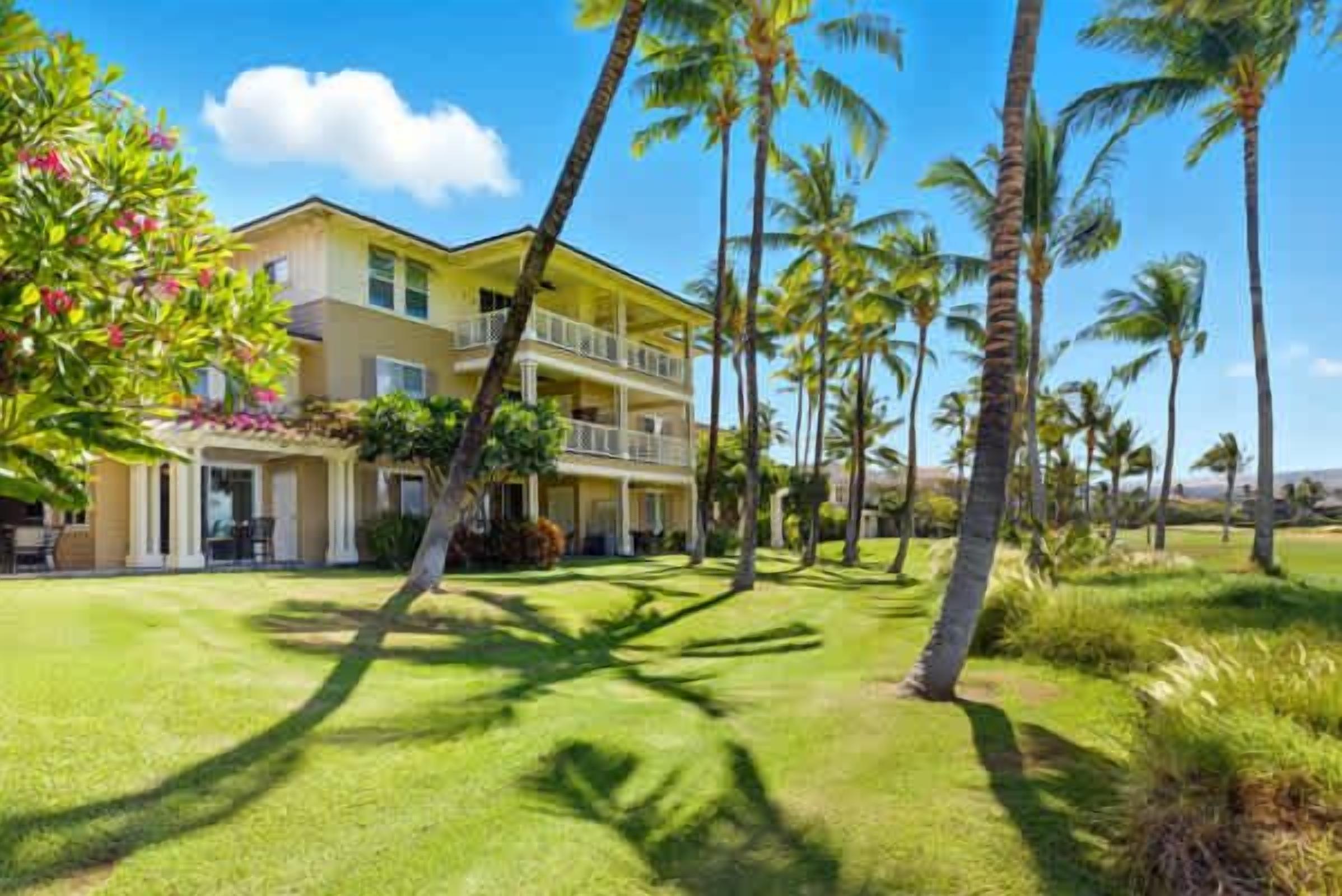 A two-story hotel with a balcony on the second floor, surrounded by palm trees and a well-maintained lawn.