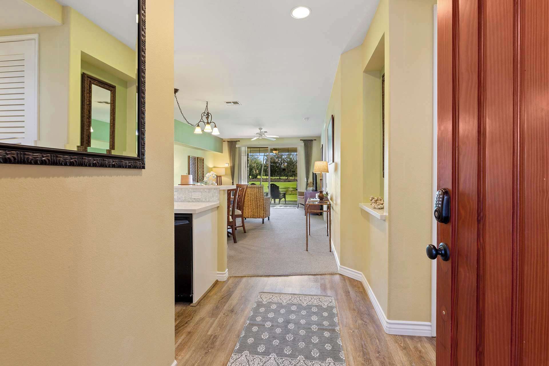 A hallway leading to a dining area with a ceiling fan, a wooden door, and a rug.