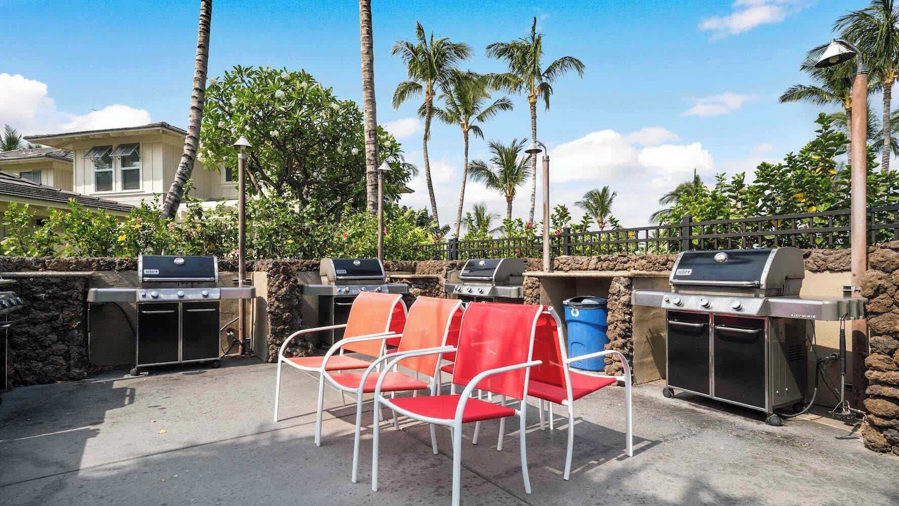 An outdoor patio with barbecue grills, red chairs, and palm trees.