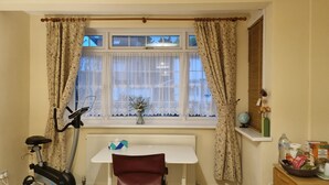 A room with a window, radiator, exercise bike, table, chair, and a shelf with items. - Beautiful Clean Double Room (Harrow)