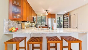 A modern kitchen with wooden cabinets, a marble countertop, and a built-in island with bar stools. - Country Club Villas Golf, A/C & Oceanview (Kailua-Kona)