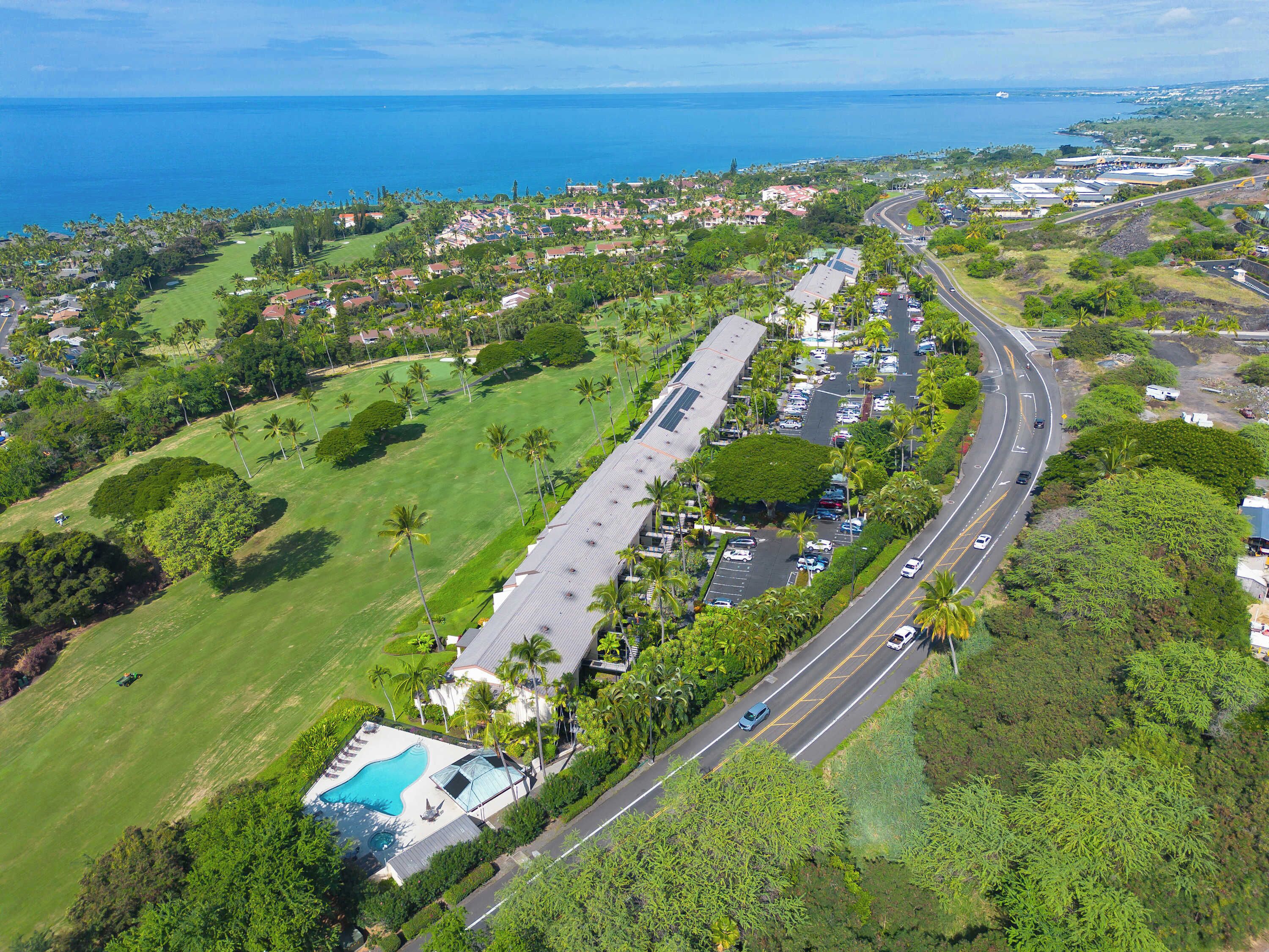 An aerial view of a coastal property with a swimming pool, a road, and surrounding greenery.
