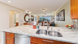 A modern kitchen with a marble countertop, double sink, and wooden cabinets. - Country Club Villas Golf, A/C & Oceanview (Kailua-Kona)