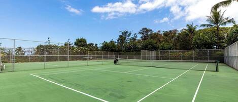 A tennis court with a net, surrounded by a fence and trees.