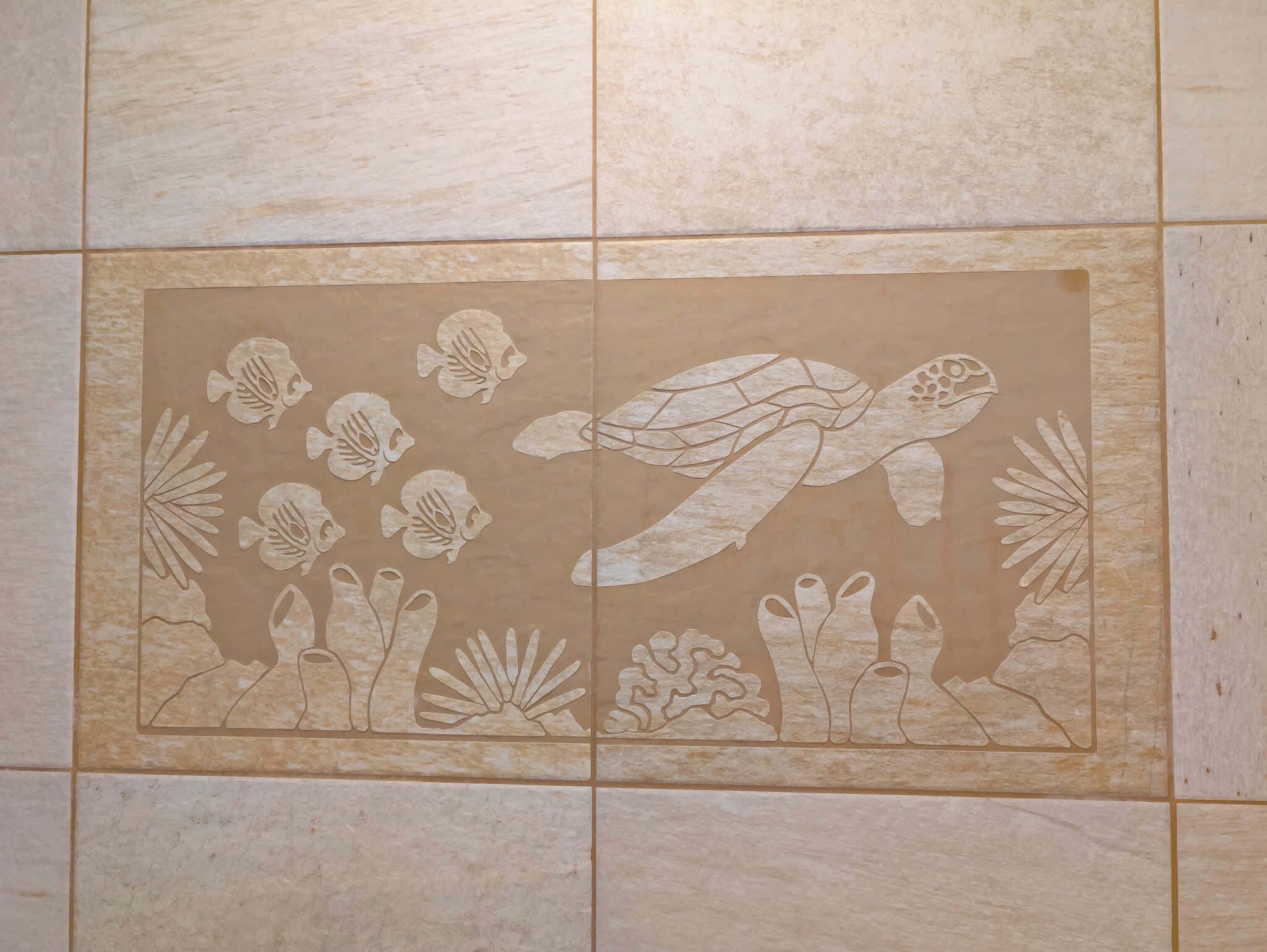 A bathroom with a large mirror and a tiled wall featuring a sea turtle and fish design.