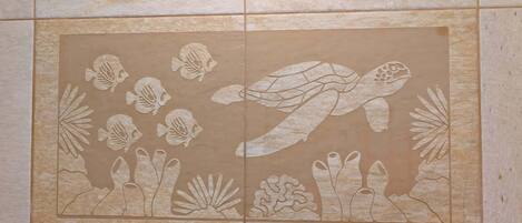 A bathroom with a large mirror and a tiled wall featuring a sea turtle and fish design.