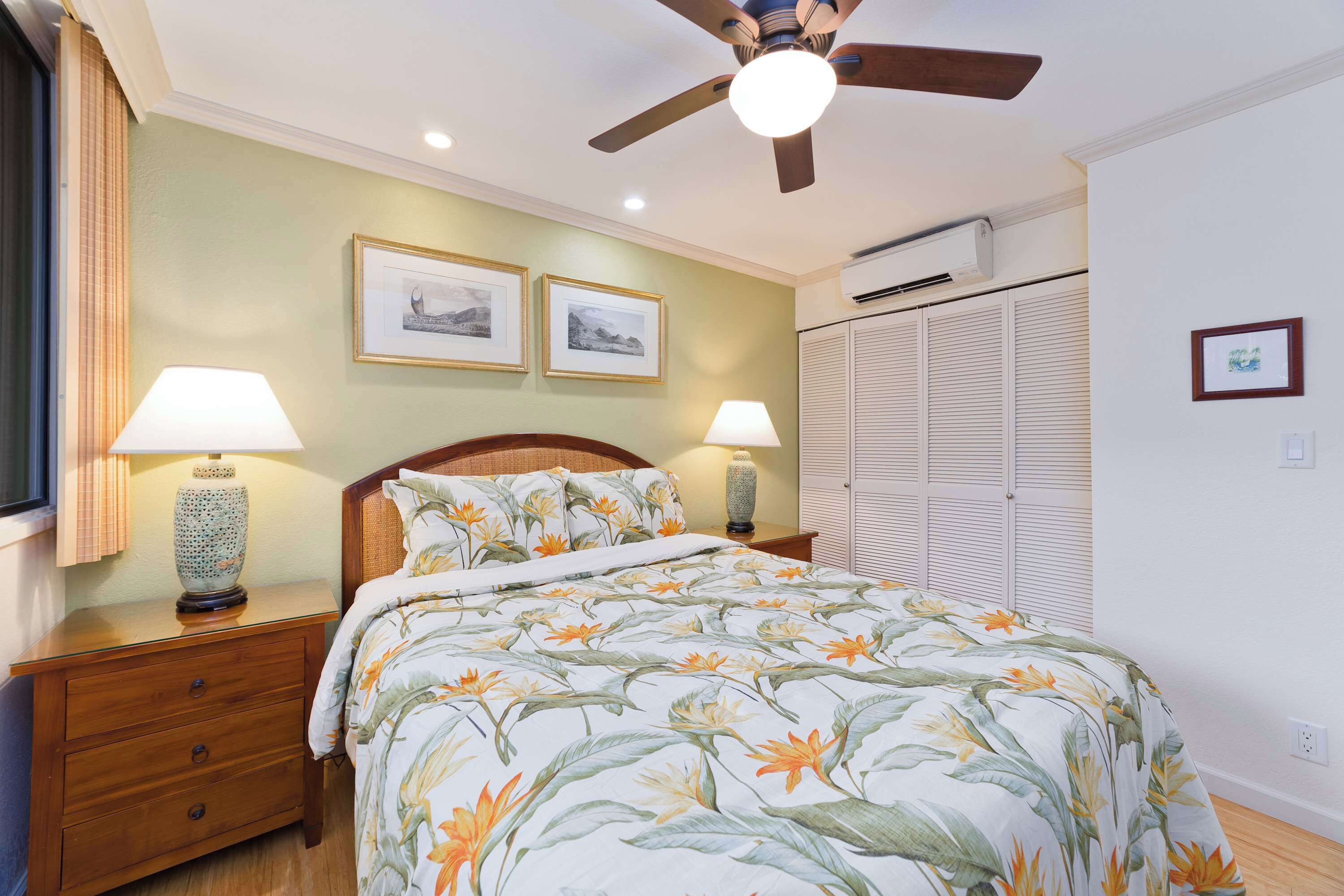 A bedroom with a bed, two bedside lamps, a ceiling fan, and framed pictures on the wall.