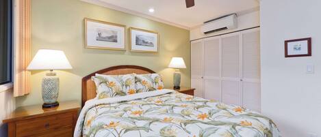 A bedroom with a bed, two bedside lamps, a ceiling fan, and framed pictures on the wall.