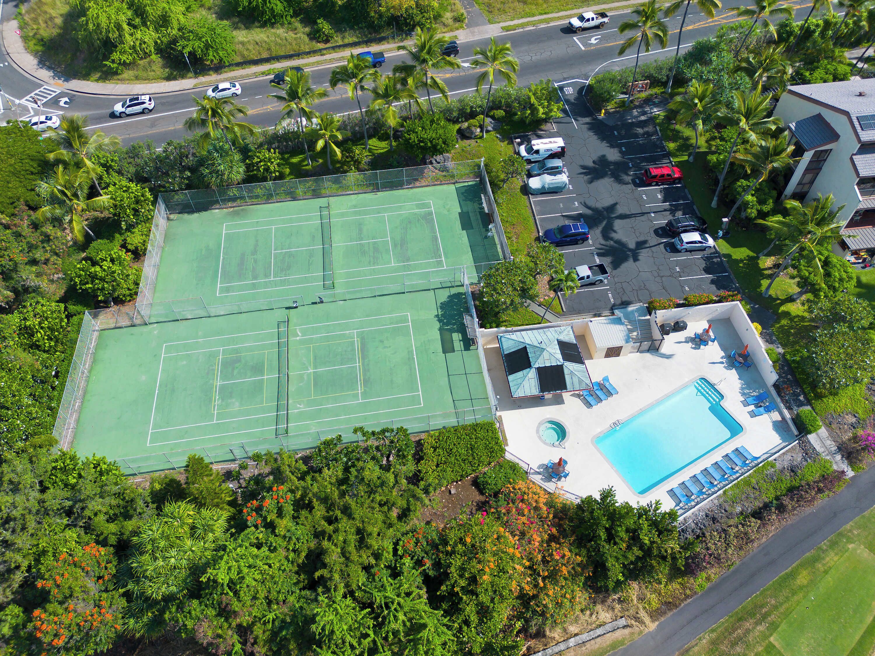 Vue aérienne d’un court de tennis situé à côté d’une piscine, avec des chaises longues et un espace aménagé au bord de la piscine.
