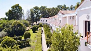 A row of white buildings with red-tiled roofs, surrounded by lush greenery and trees. - Elena Mare (Lesvos)