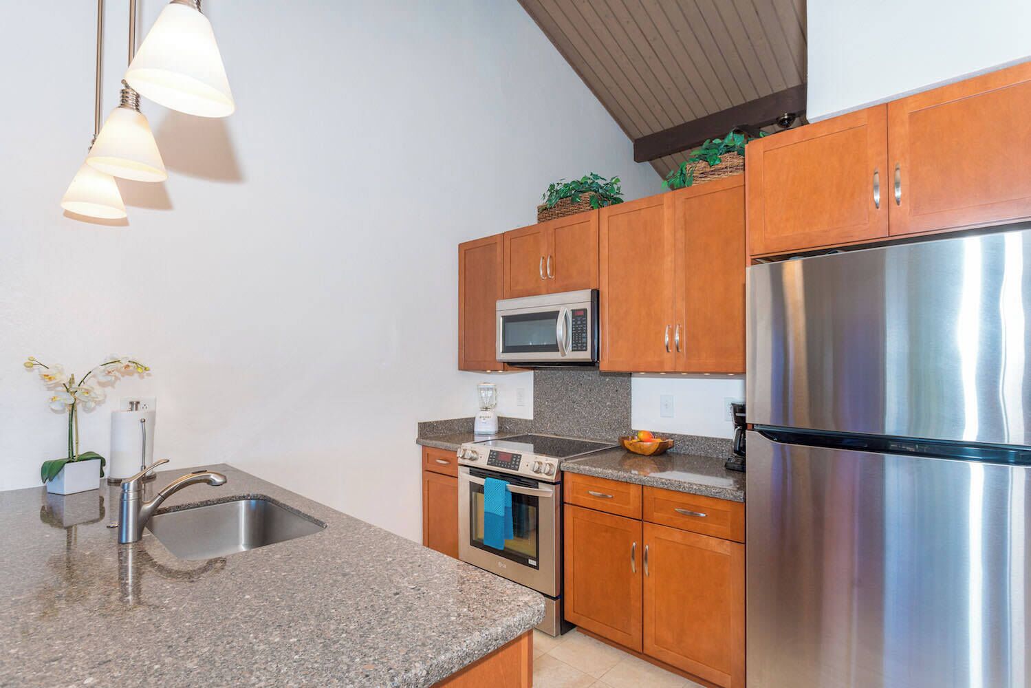 A modern kitchen with granite countertops, stainless steel appliances, wooden cabinets, and pendant lighting.