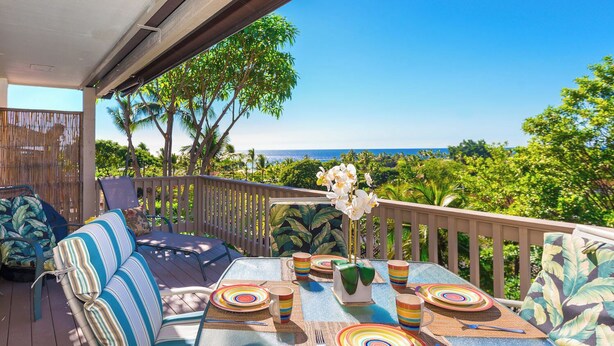 Eine Terrasse mit einem Glastisch, gedeckt für ein Essen, umgeben von gestreiften Lounge-Stühlen und Blick auf eine tropische Landschaft sowie das Meer.