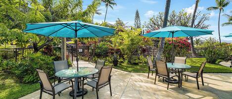 An outdoor patio with two round tables, each surrounded by four chairs and a large turquoise umbrella.