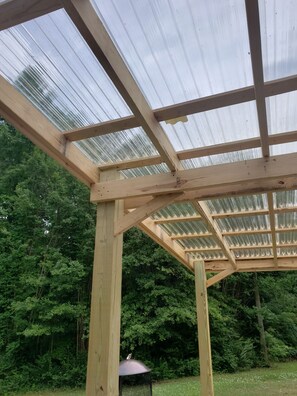 Una estructura de madera con techo transparente, rodeada de abundante follaje verde.